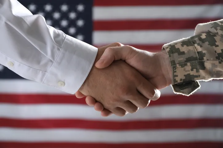 a veteran shaking a hand in front of an american flag